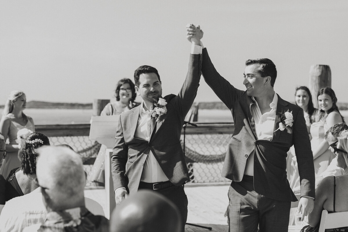 Just married, the two grooms kiss joyfully during their Castaway Cay wedding ceremony with guests cheering.