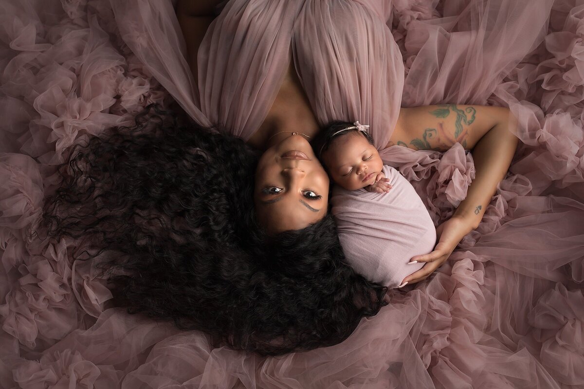 Mother and newborn baby girl laying on flowing mauve fabric during a Dallas newborn photography session