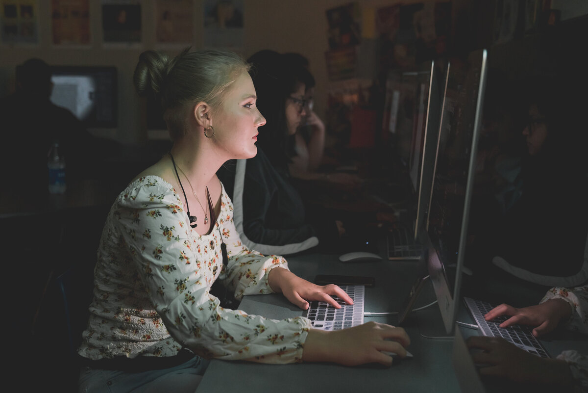 Female teenage student working on a computer in a dark classroom
