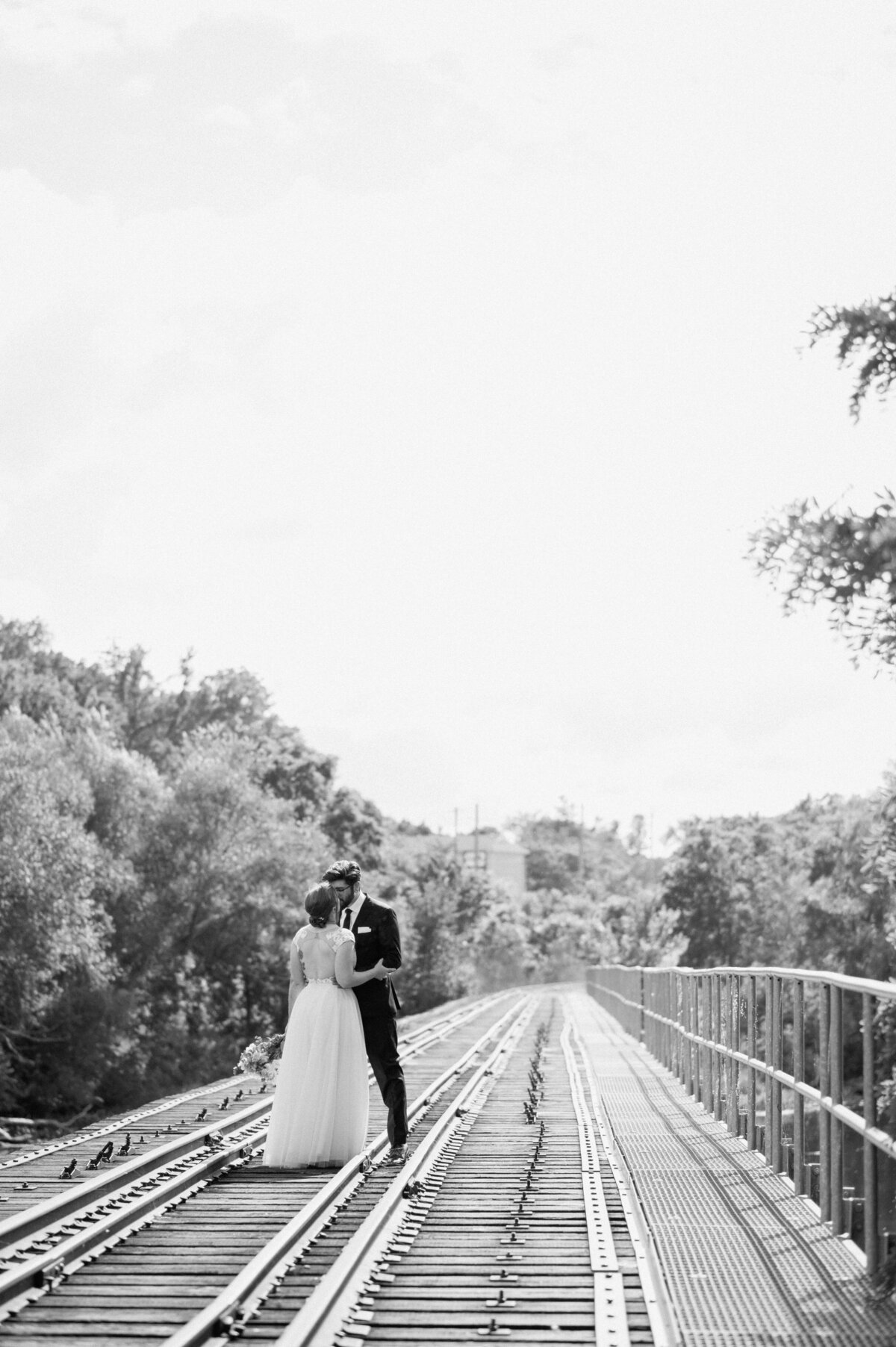 bride and groom kiss on the train tracks