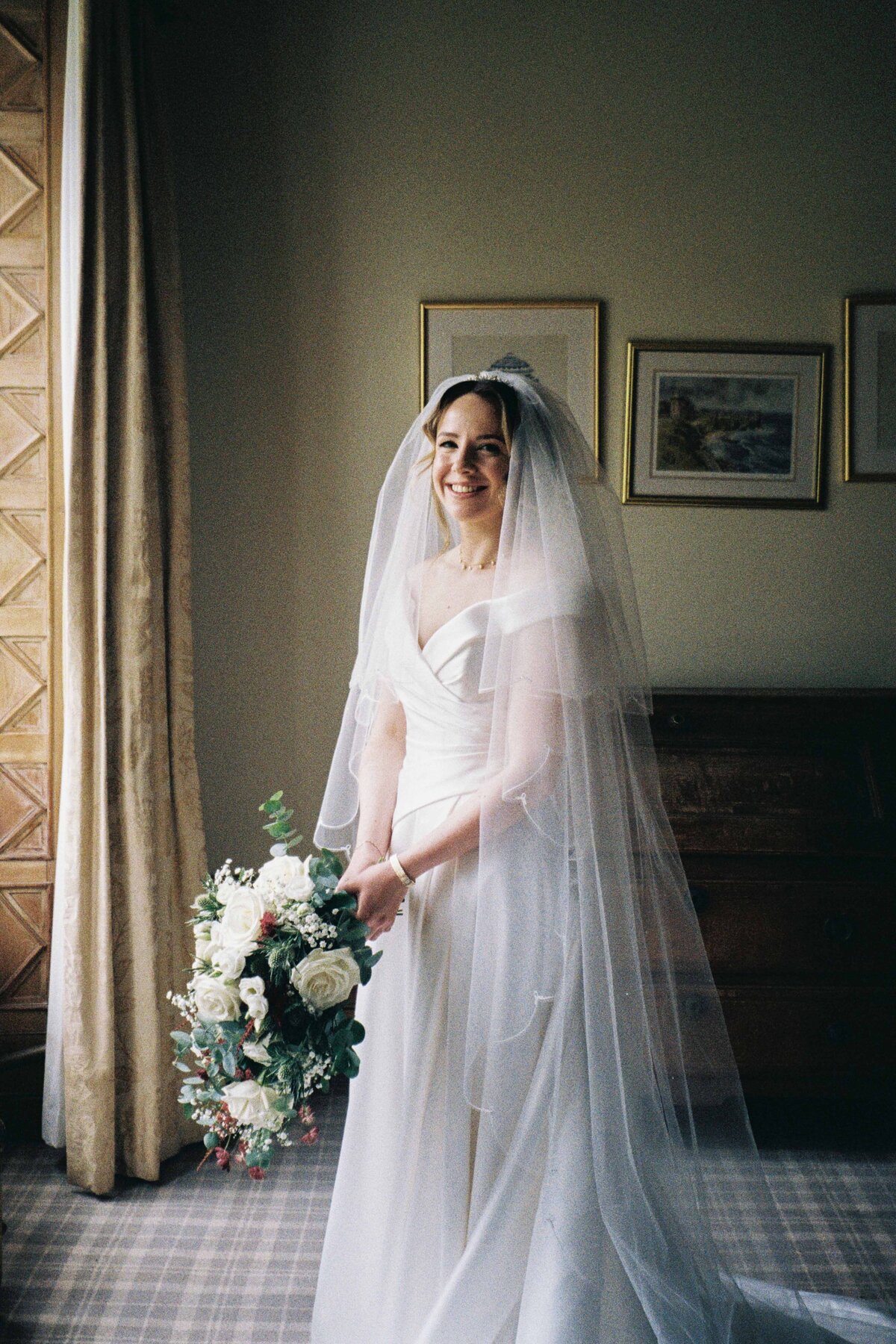 A portrait photograph of a bride standing by a window in Meldrum House in Aberdeenshire.