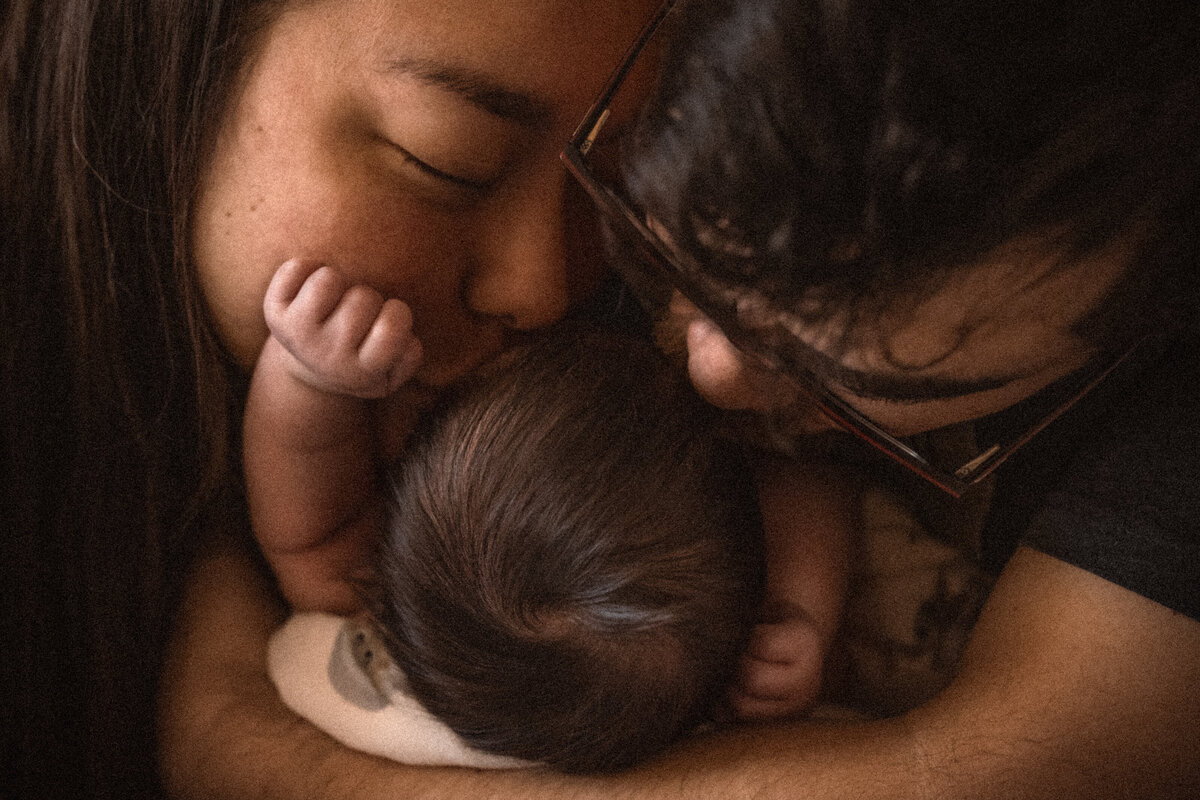 mother and father kissing newborn baby