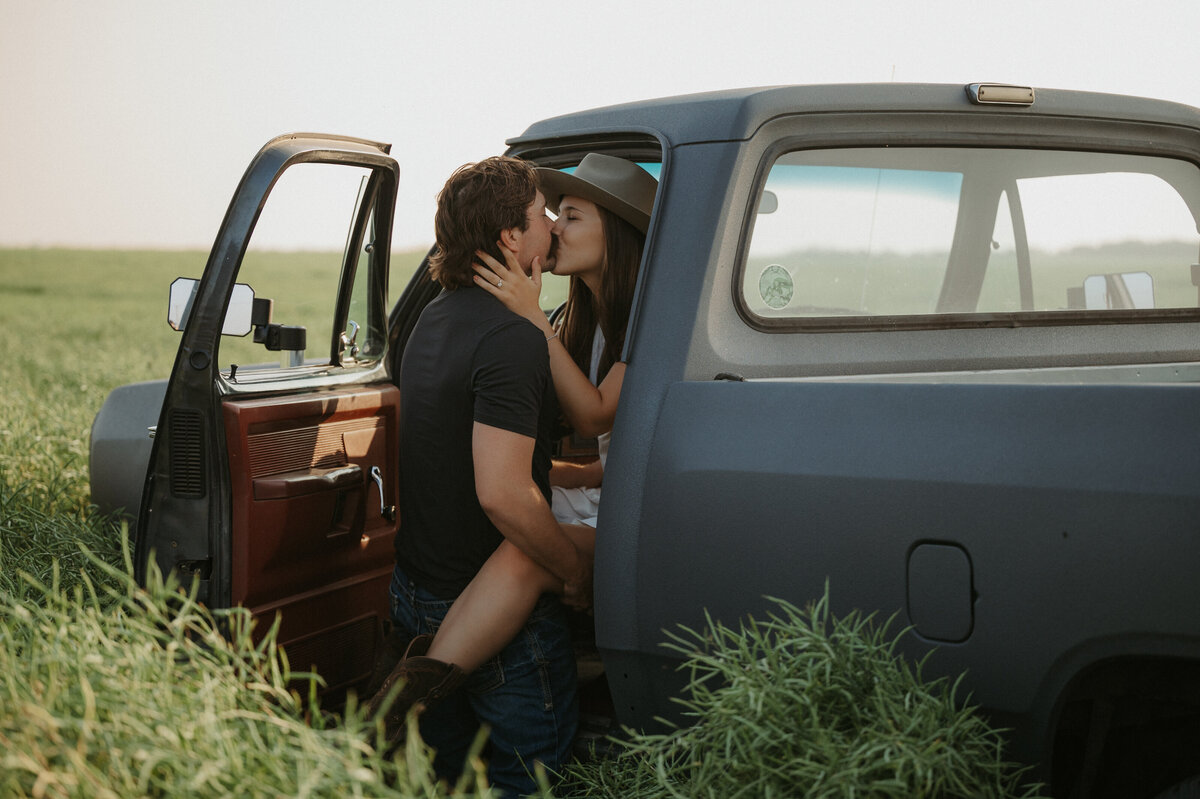 Outdoor summertime photo of couple kissing outside of an old truck in Alberta