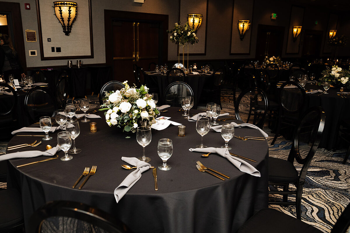 Wedding reception setup with black table cloths, gold flatware, and grey silk napkins.