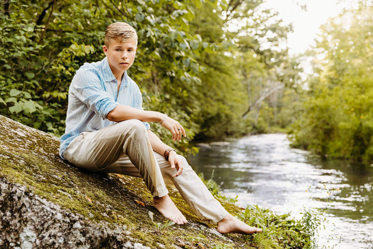 Senior boy sitting on a large rock in a creek by Ashley Kalbus