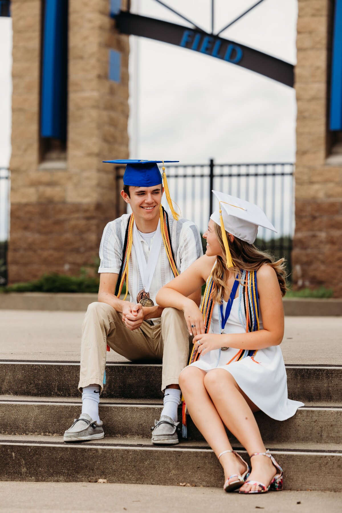 High school sweethearts at graduation on steps of school stadium.