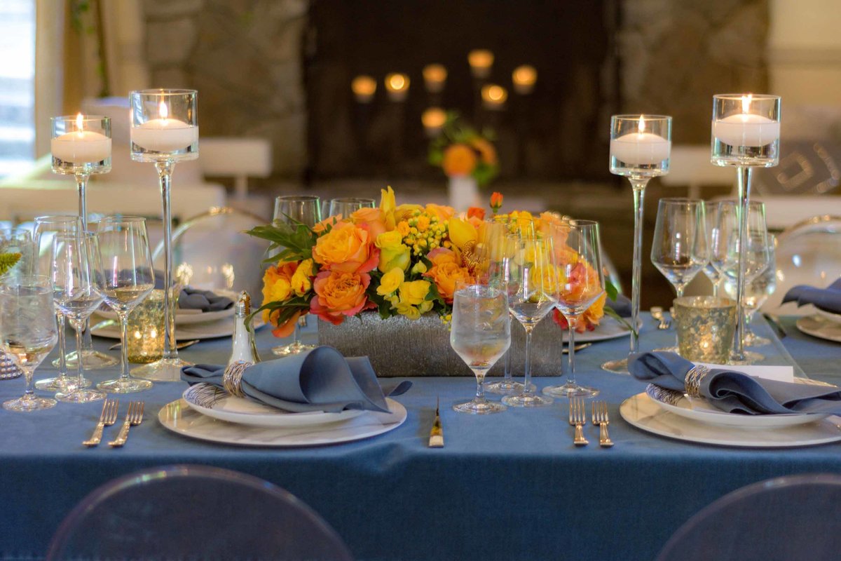 centerpiece of orange and yellow roses, orange calla lilies, blue linen, in front of fireplace