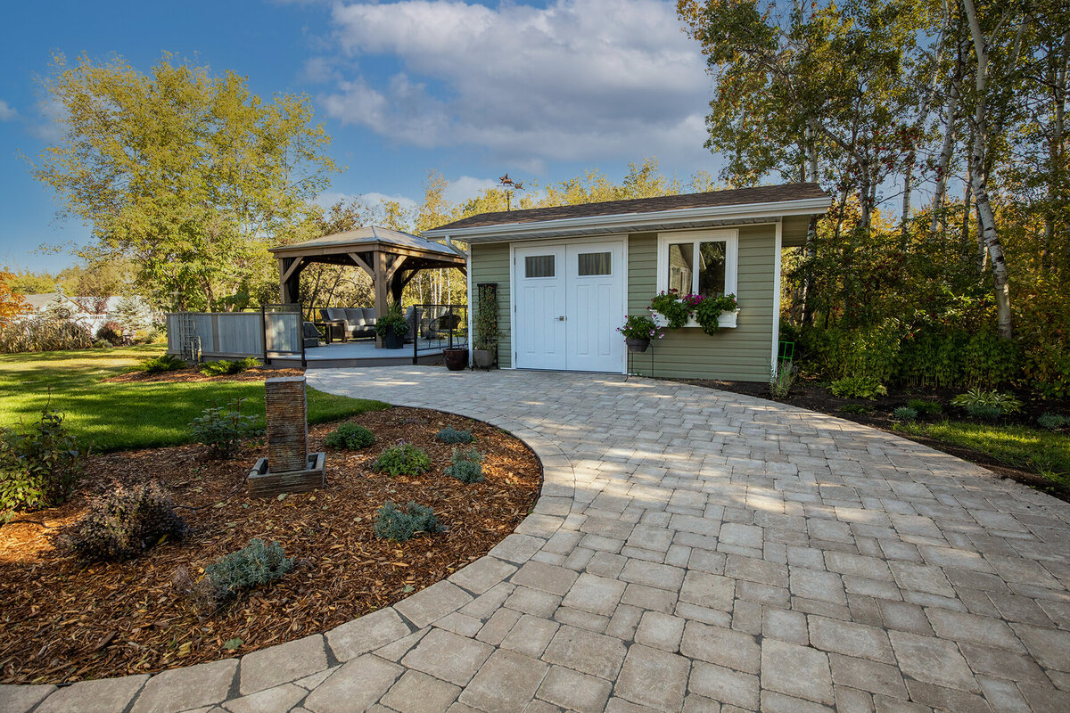 backyard with cedar mulch bed with perennials and a winding path leading to a utility shed and a pergola for a seating area under the trees