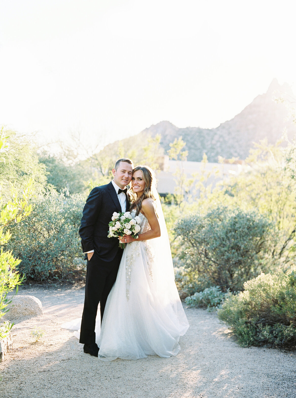 A romantic moment captured between the bride and groom in a breathtaking desert landscape, surrounded by lush greenery and mountain views.