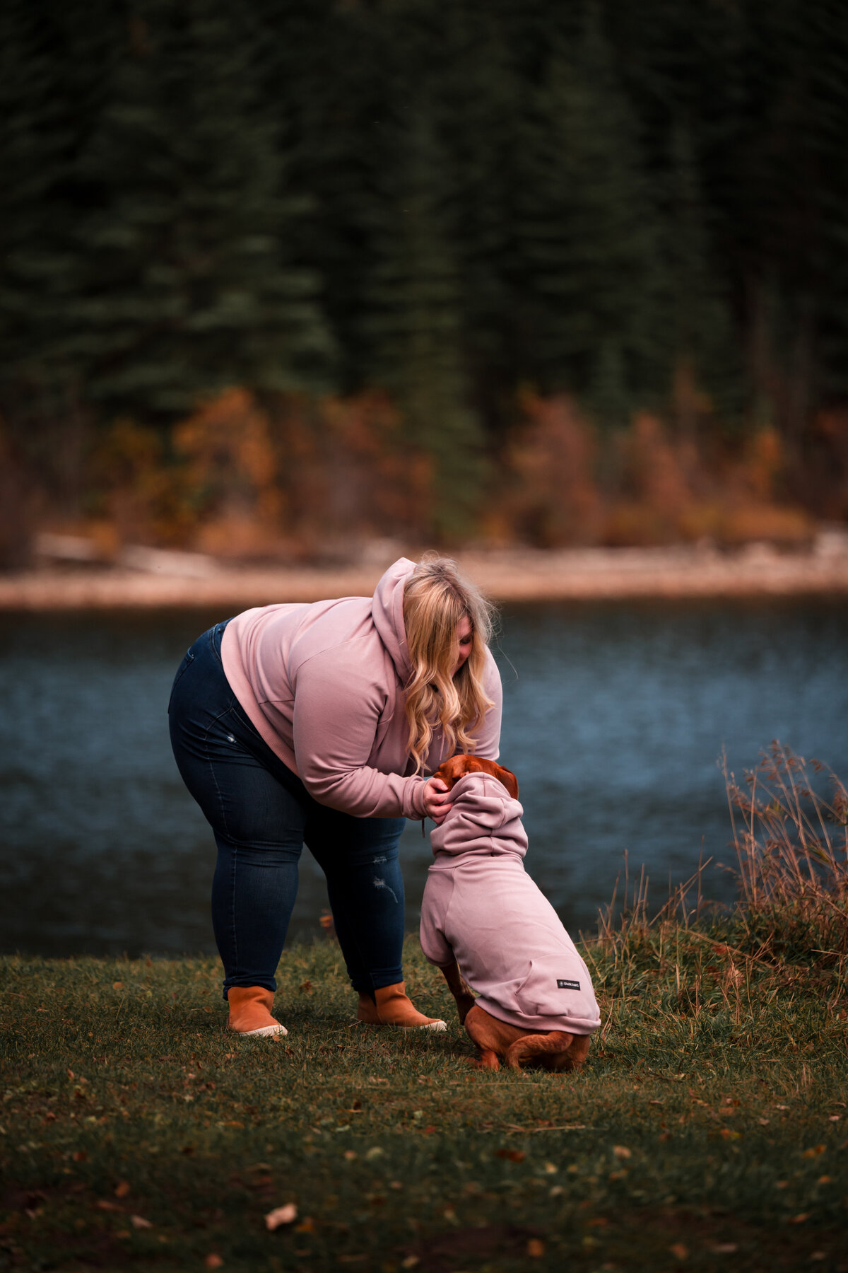 woman leans down and holds onto dog both have matching sweaters