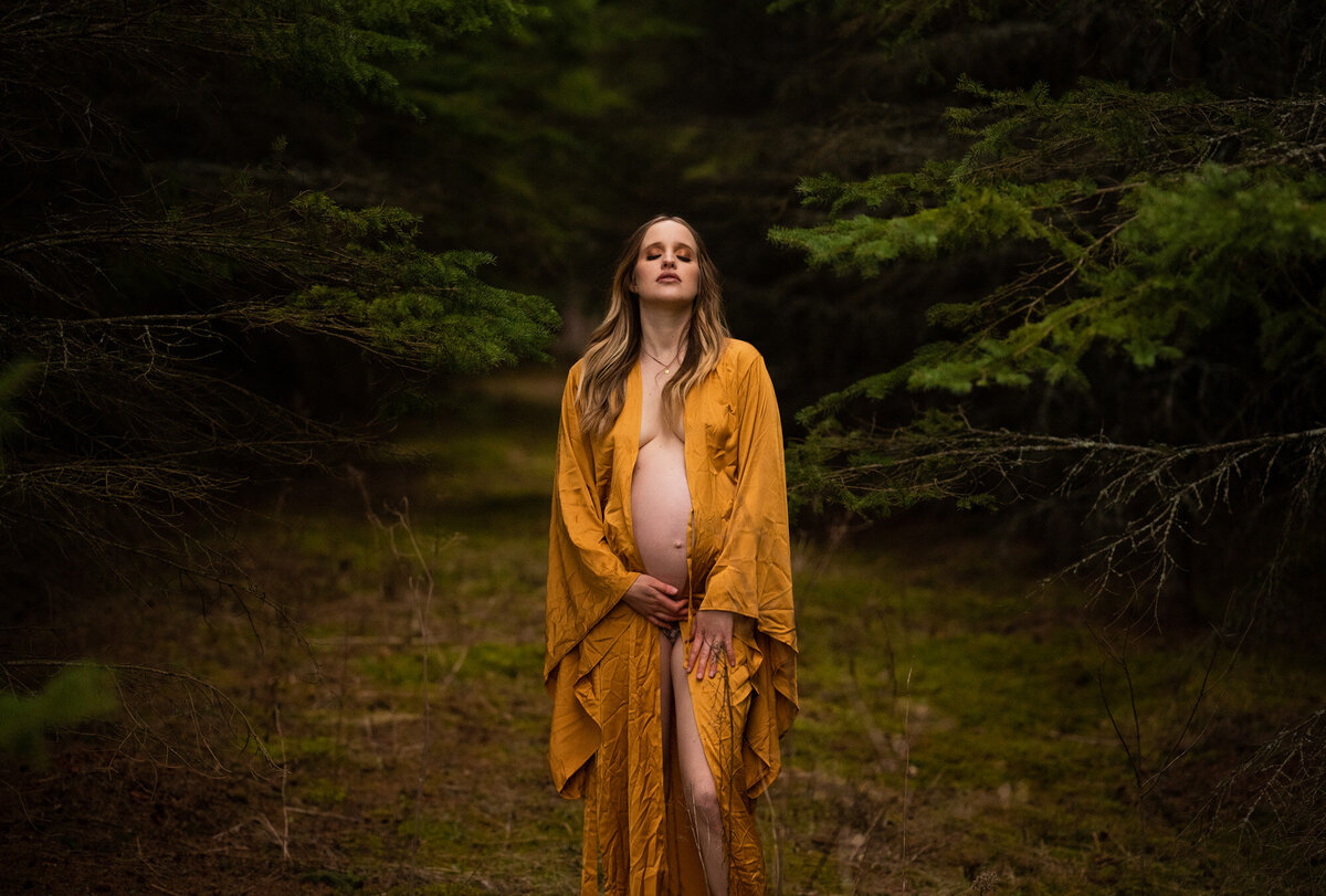 Pregnant Mom looking up at the sky wearing a gold robe and bear belly showing.