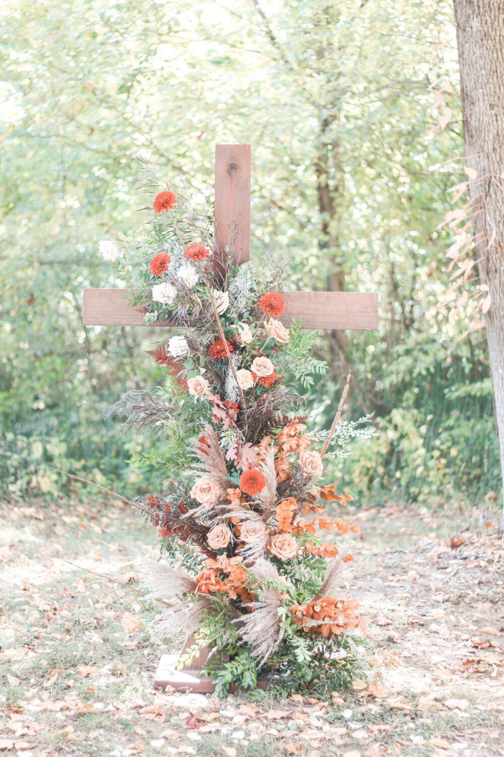 Wooden cross adorned with autumn flowers and greenery