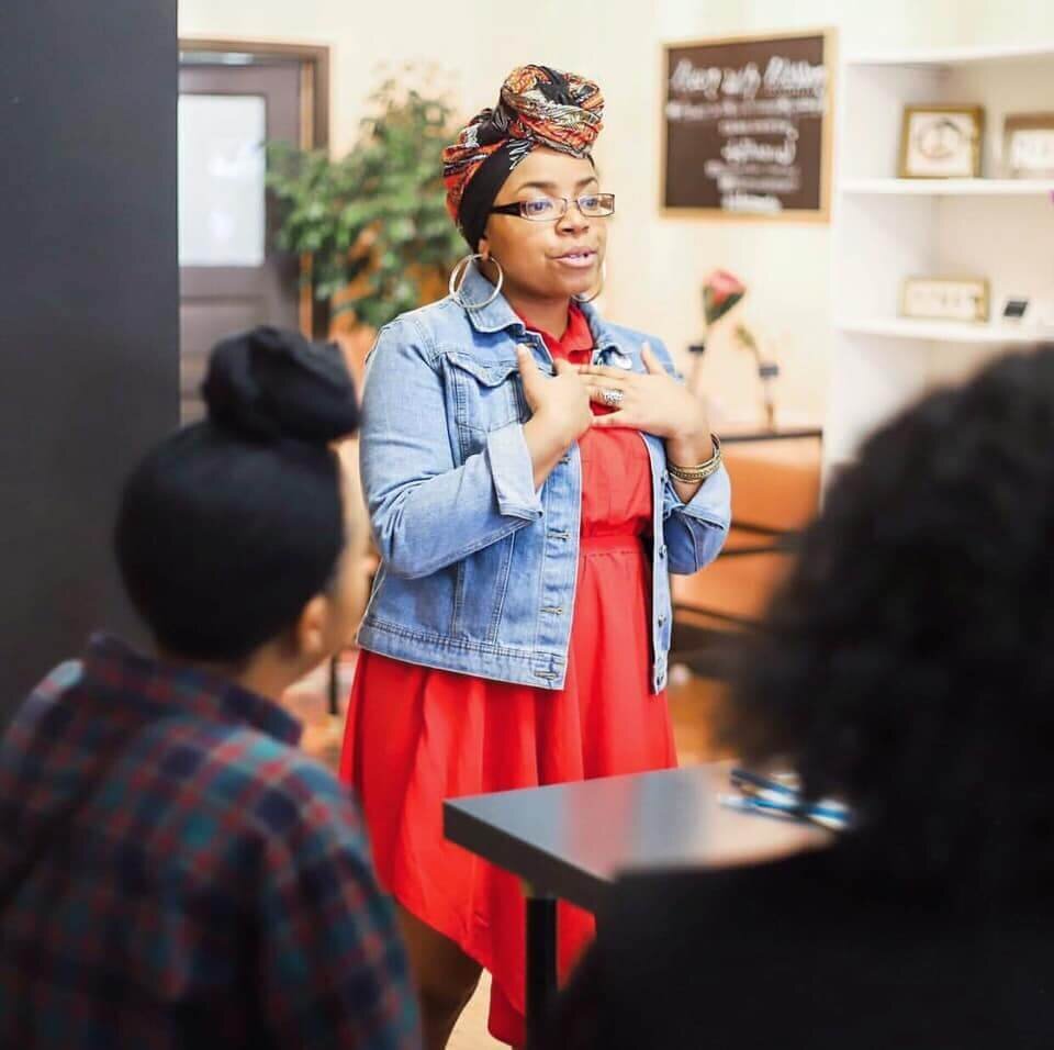 African American woman in red dress and jean jacket speaking at an event to other women