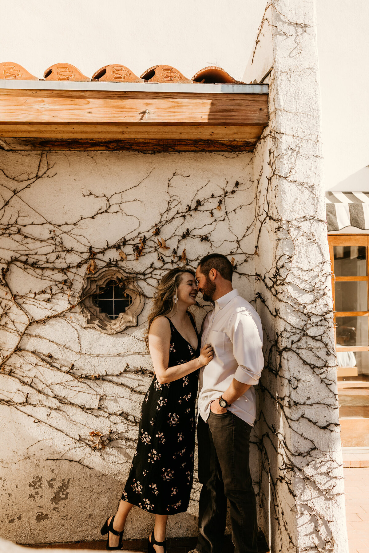 engaged couple leaning on a white wall with vines