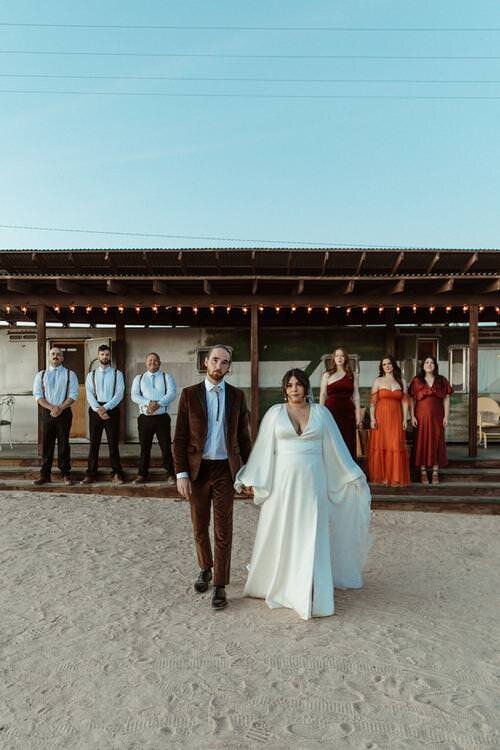 Bried-and-groom-holding-hands-with-their-entourage-behind-them,-captured-by-From-The-Daisies.jpg