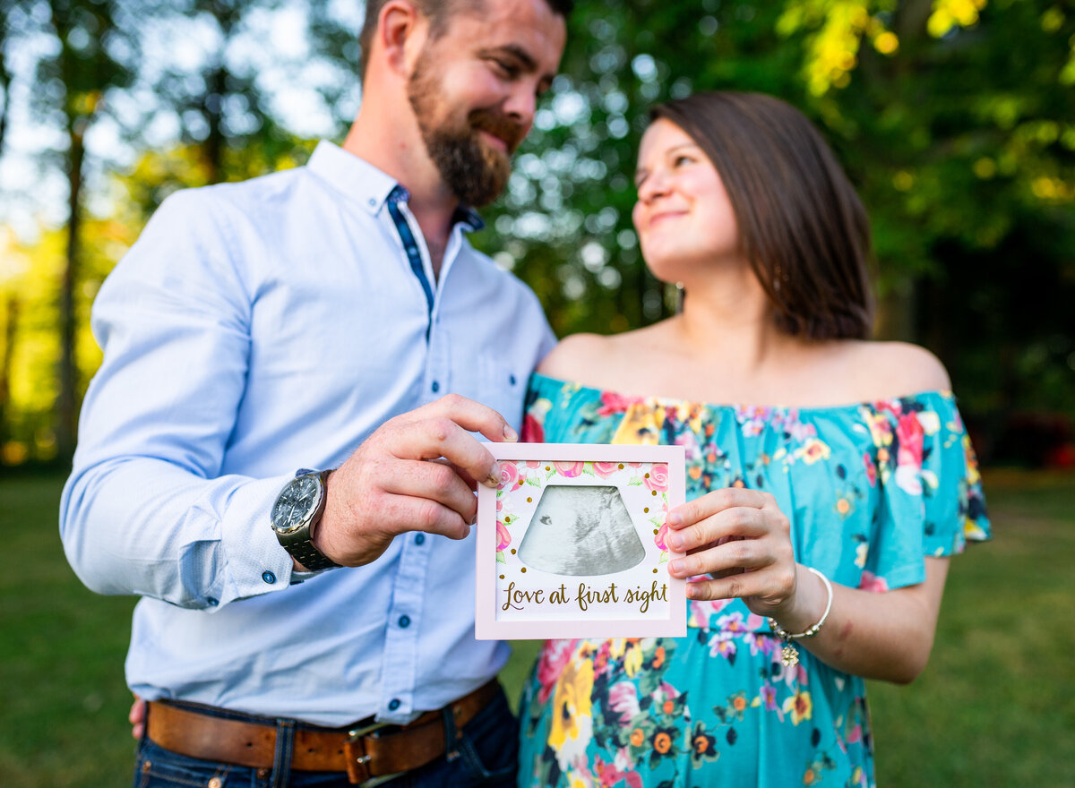 Couple lovingly holding a framed ultrasound photo that says “Love at first sight"