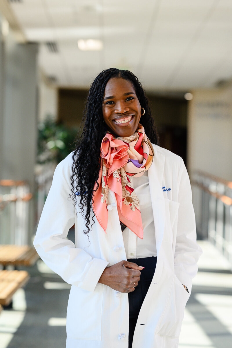 A brand photographer takes a picture of a Denver black woman doctor standing in a hospital with lots of windows for a branding photography session for branding pictures.