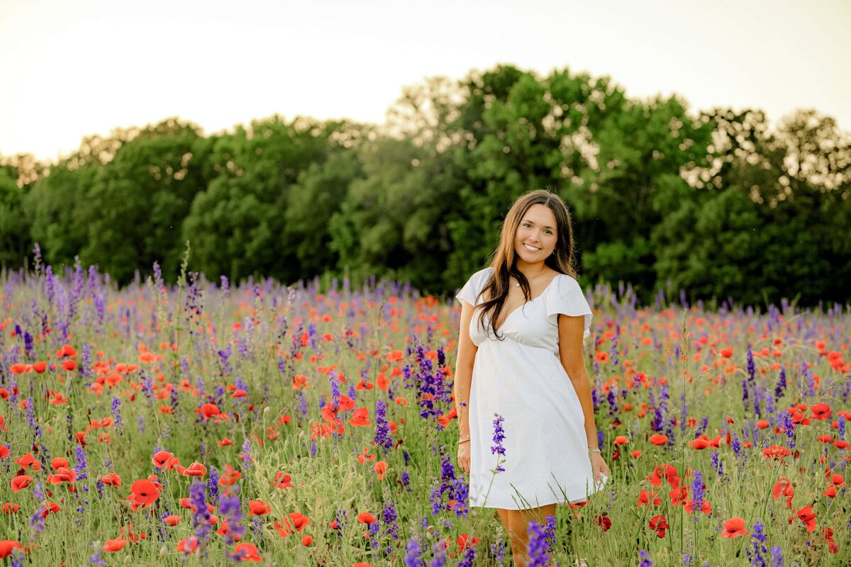 A grad stands in a flower field in a white dress during her spring senior session.