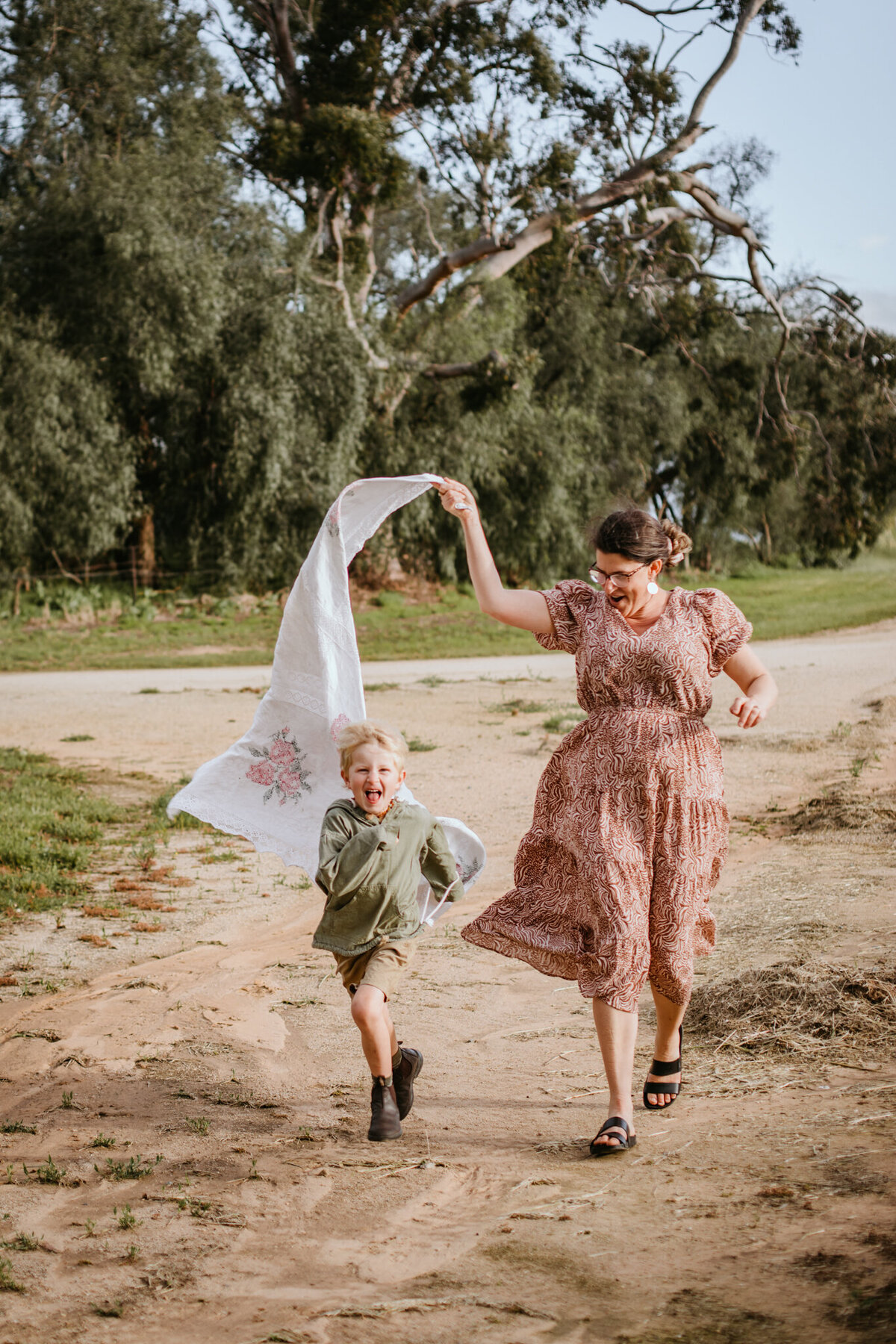 Fun moment as mom and son run on a sandy road with a white linen waving in the wind. 