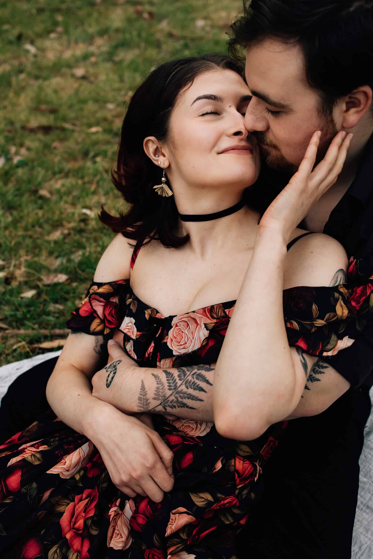 Woman reaching hand back to man's face, his arms around her, as the sit snuggled together during outdoor couples photoshoot, And So I Don't Forget Photography