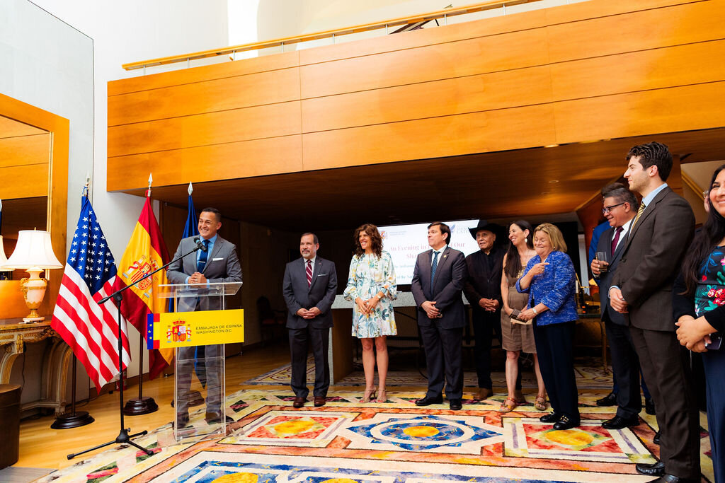 A man speaks into a microphone while others stand around.