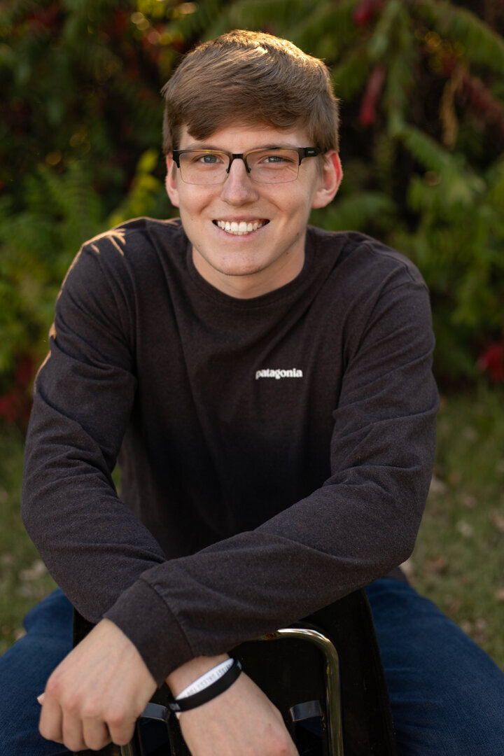A senior guy sitting on a chair backwards looking at the camera smiling in Lawrence, KS