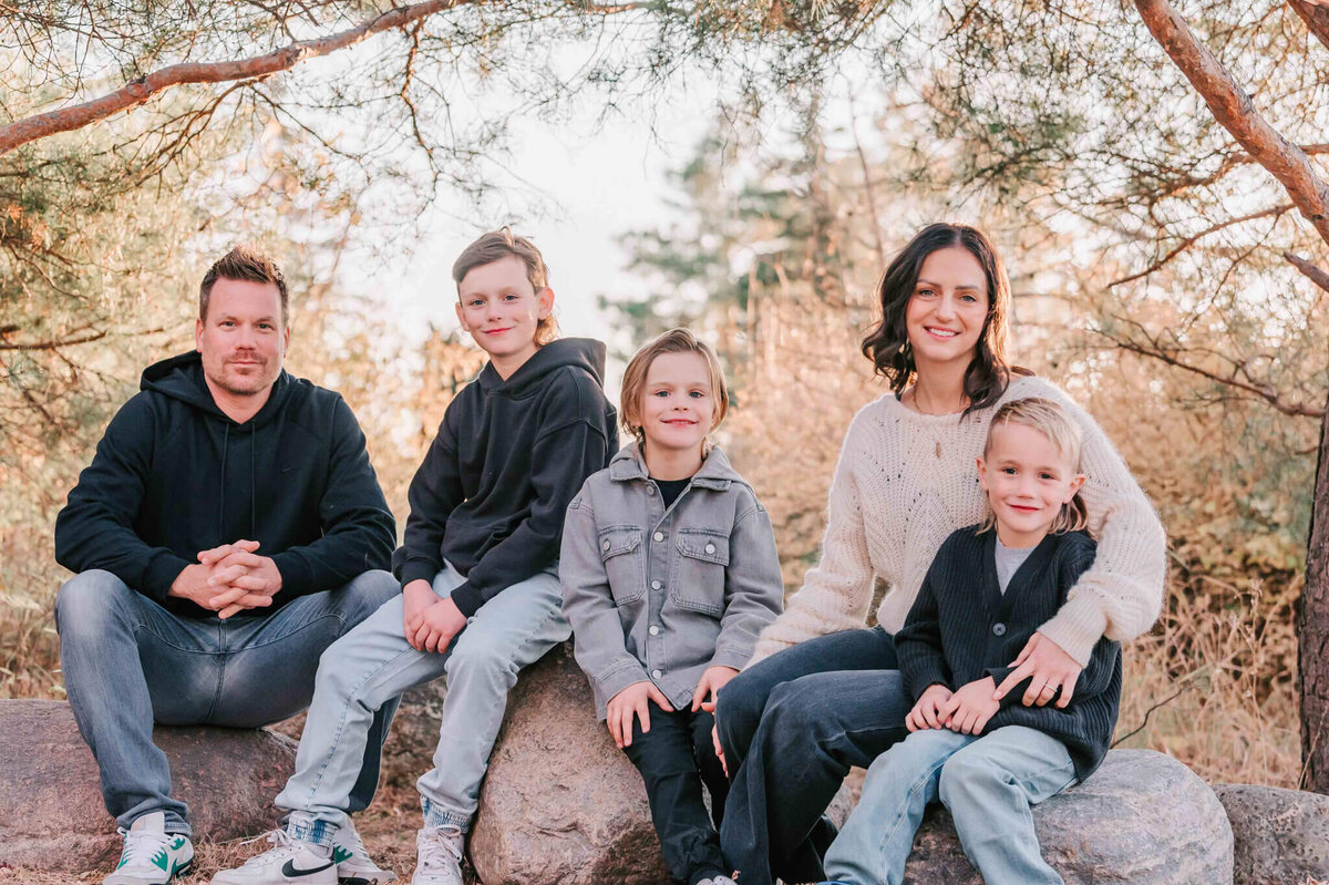 Family of 5 sit on some rocks in the trees. 