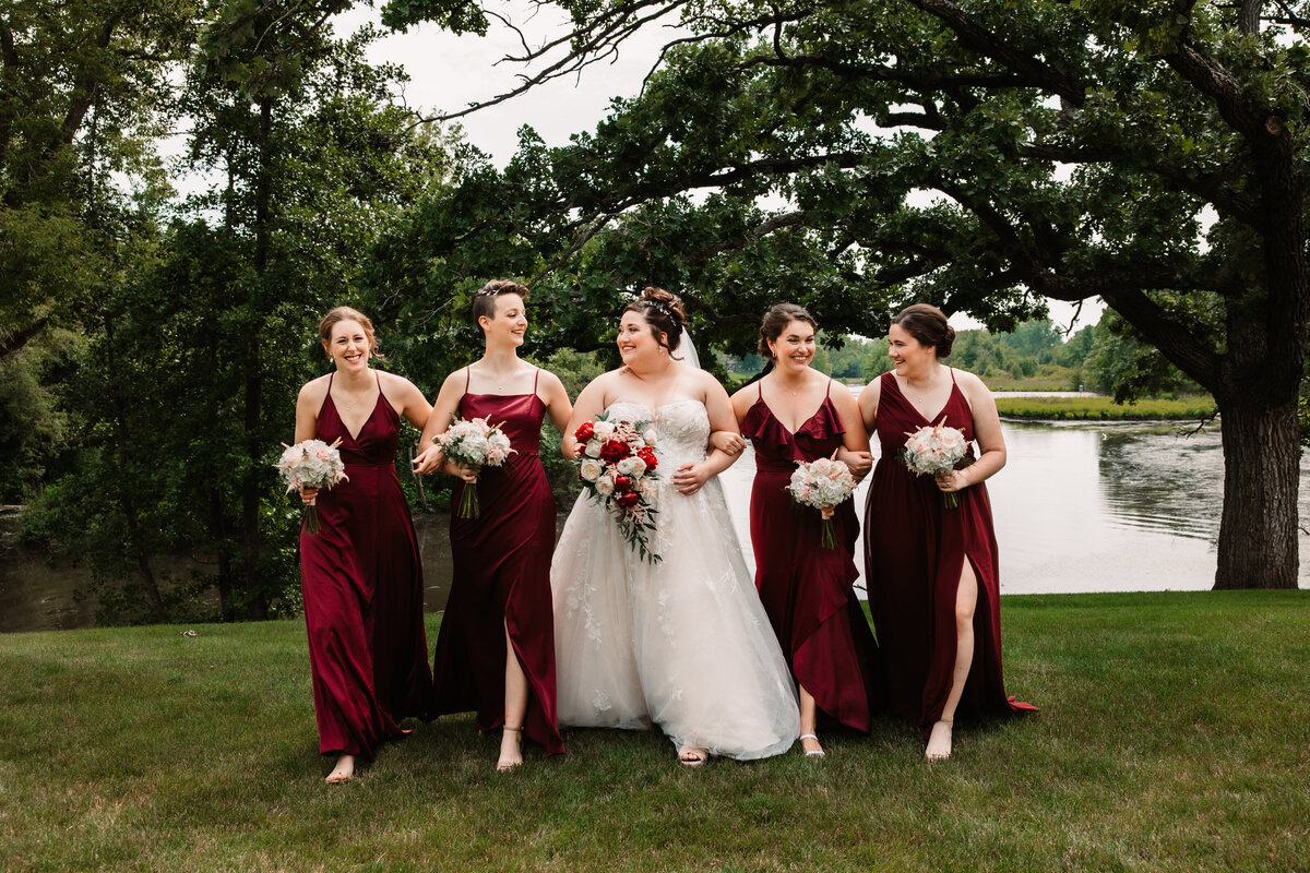 A bride laughs while walking with her bridesmaids by a lake