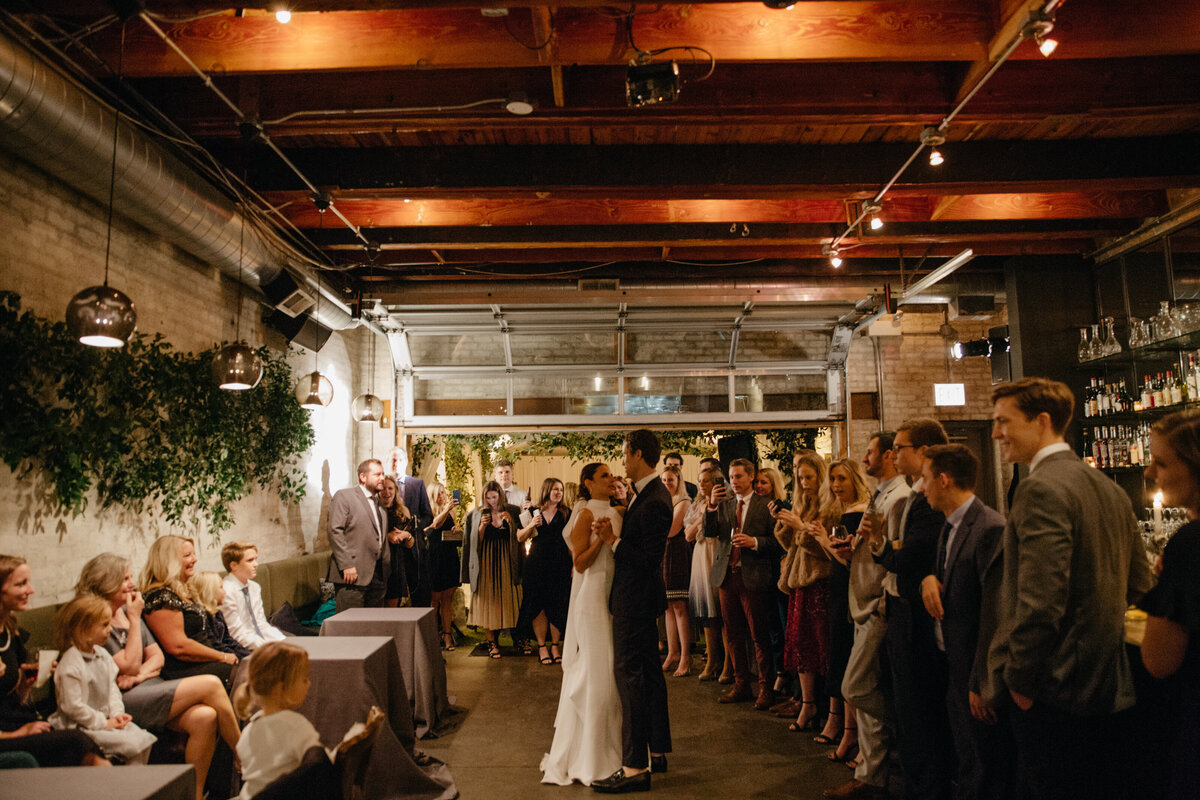 Wide angle image of bride and groom surrounded by wedding guests while enjoying first dance as newlyweds