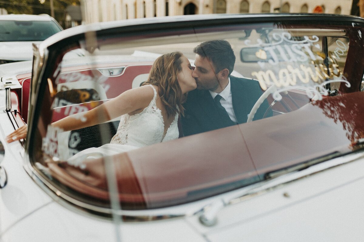 bride and groom kissing in getaway car