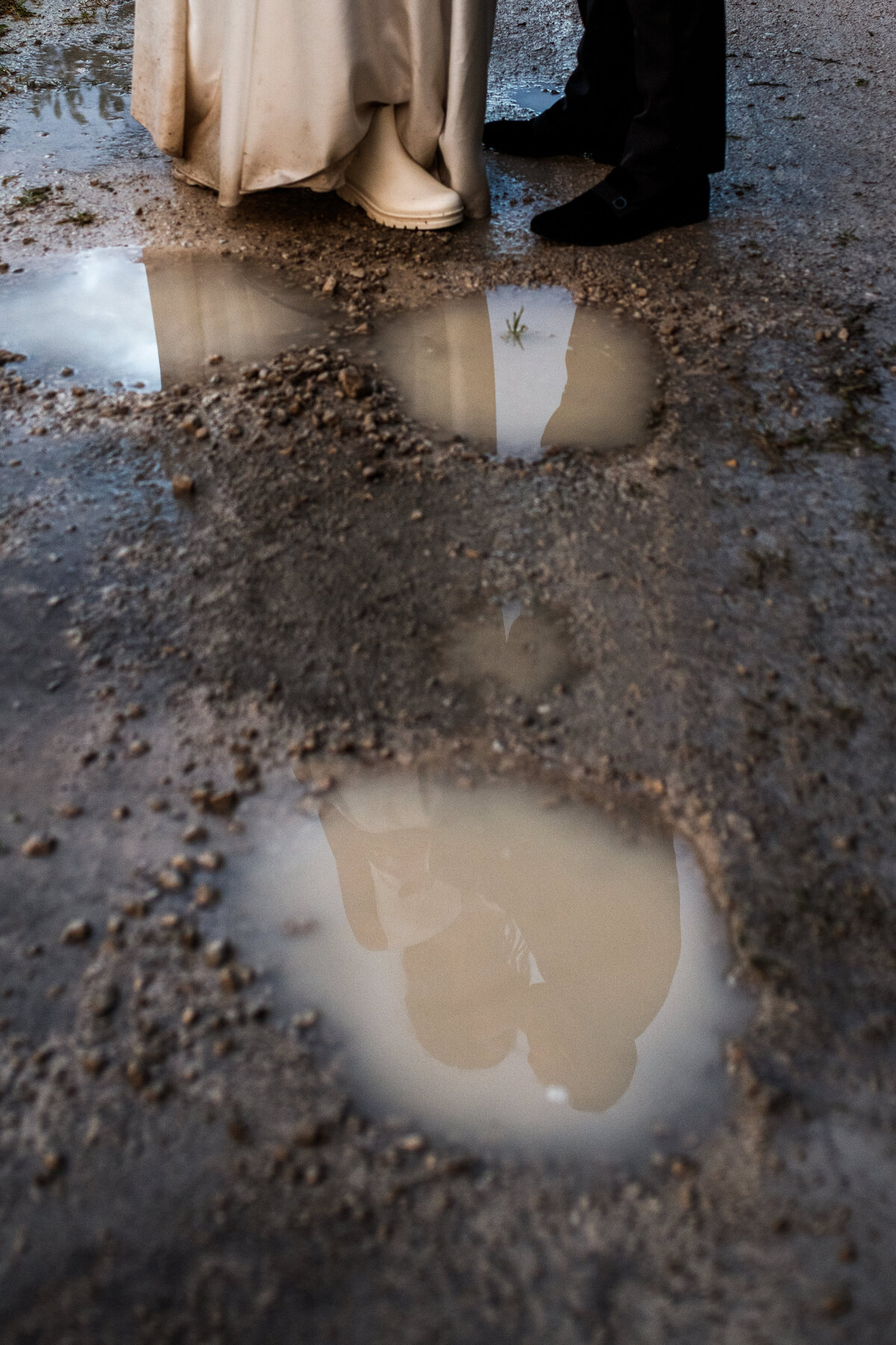 Newlyweds reflecting on a muddy puddle on the dirt road