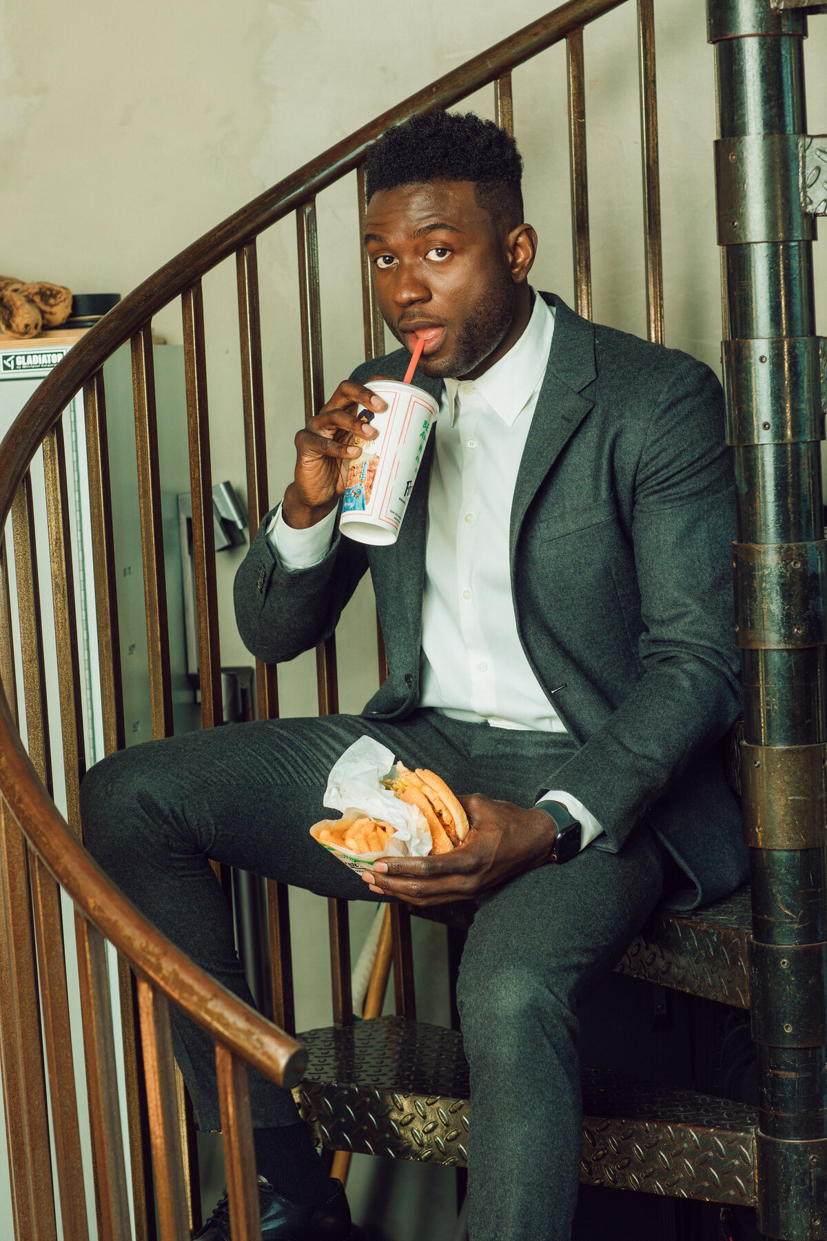 Portrait Photo Of Young Black Man In Suit Holding a Hamburger While Sipping a Drink Los Angeles