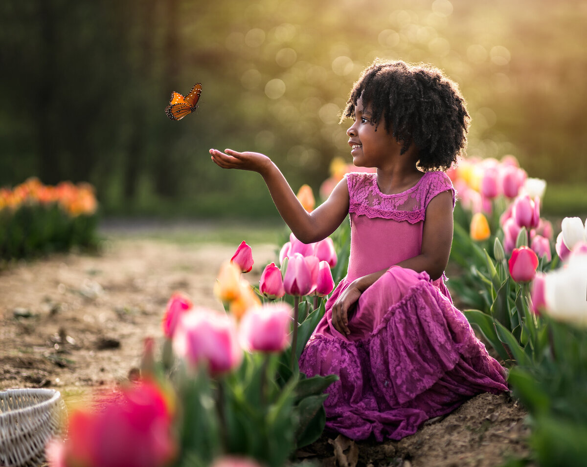 A beautiful girl in a purple dress kneels in a tulip garden near Asheville and catches a butterfly