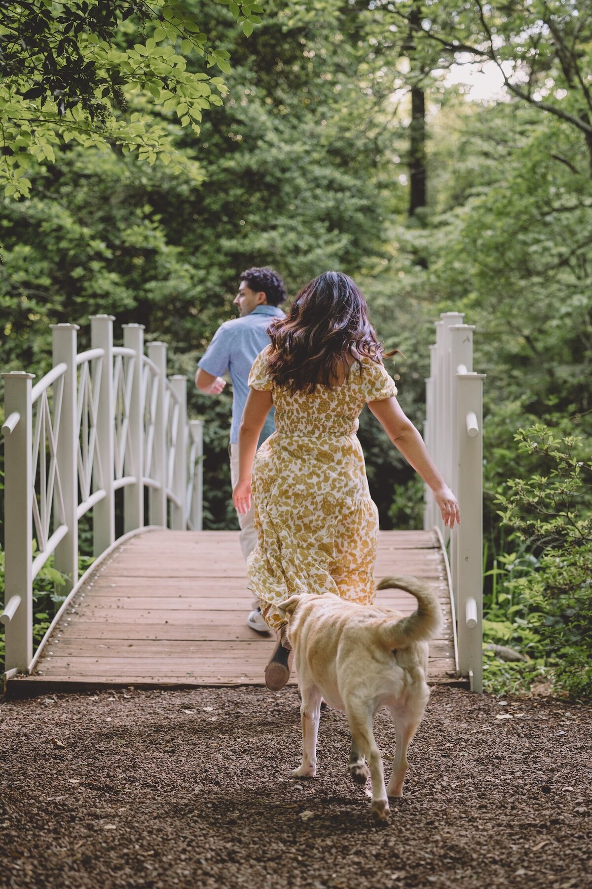 Couple walking across a white bridge with their dog.
