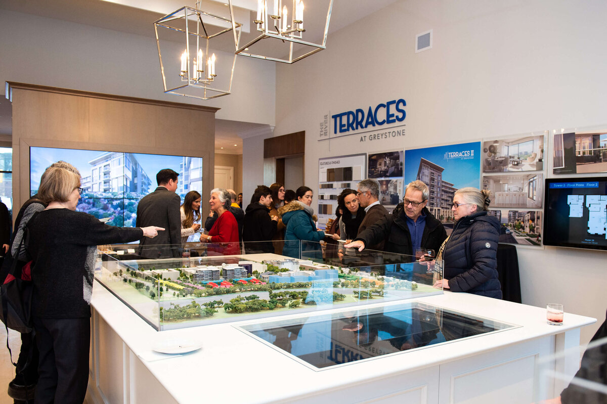 a wide angle photo of guest mingling and looking at the 3D models of homes during the eQ Groundbreaking event.  the host of eQ addressing and welcoming guests to the eQ Groundbreaking event.  Captured by Ottawa Event Photographer JEMMAN Photography COMMERCIAL