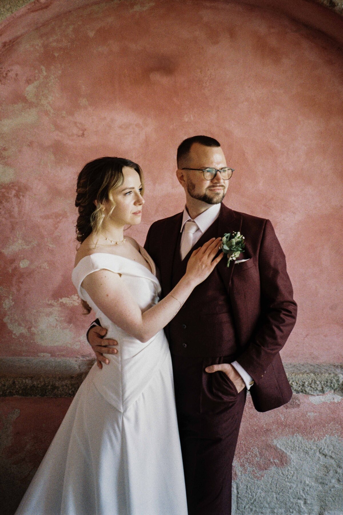 A couple stand with each other after their wedding. A large pink arch is photographed behind them. It is a 35mm film photograph.
