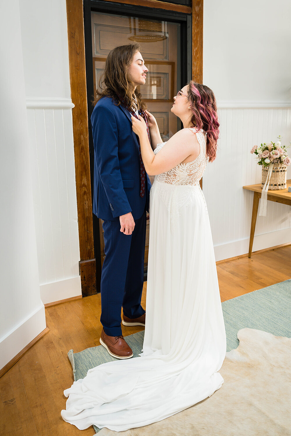 A marrier drapes her partner’s tie over his shoulder and pulls him in close as the two get ready together for their elopement in a hotel room at Fire Station One in Roanoke, Virginia.