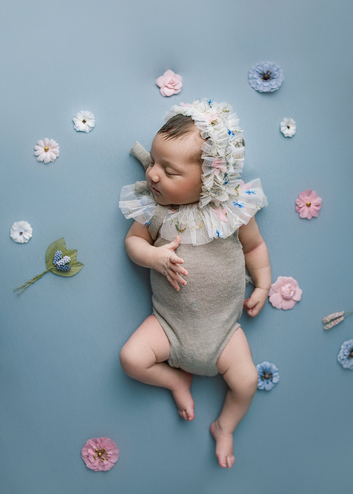 Newborn baby girl wearing grey romper laying on blue fabric during newborn session photoshoot in Franklin Tennessee photography studio