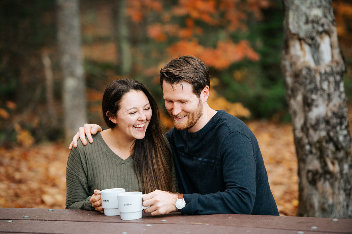 couple laughing with coffee at picnic table fall in vermont