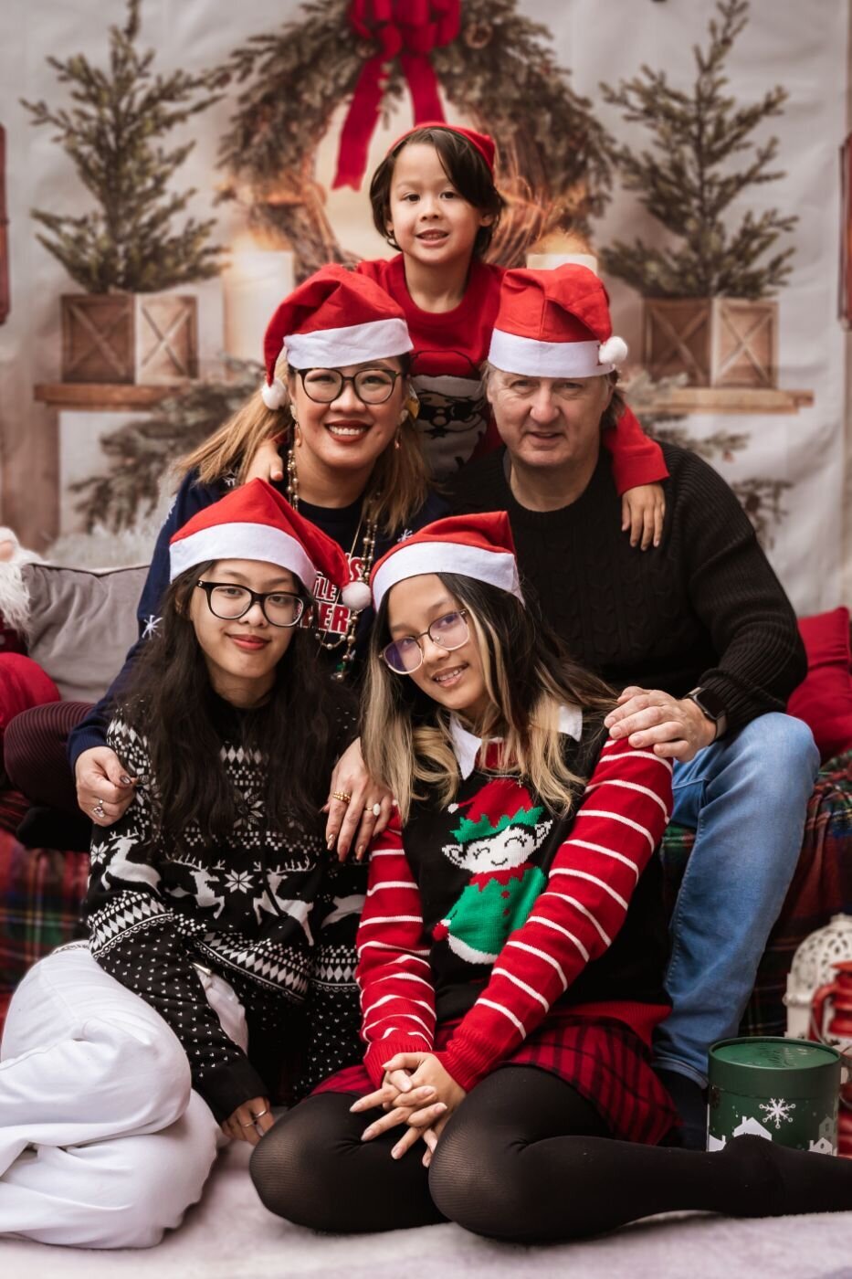 Multi-generational family in Santa hats posing together in a rustic Christmas setup.