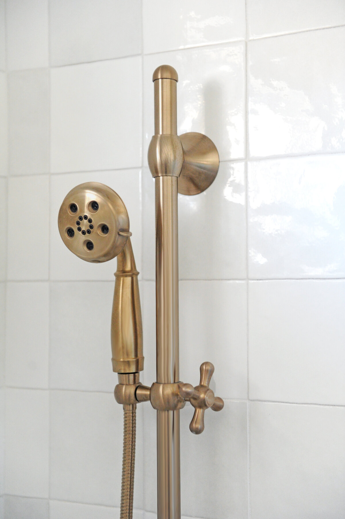 Brass  hand shower fixture mounted to tile shower wall