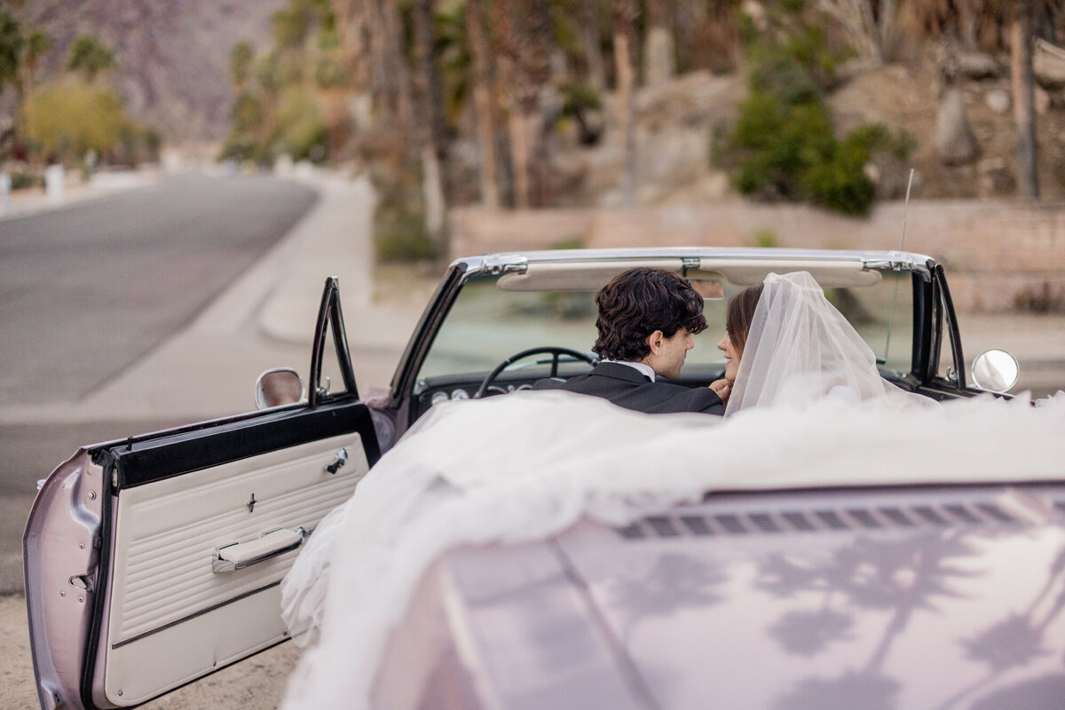Couple relaxing together on a vintage car, dressed in black and white, framed by mid-century modern scenery.