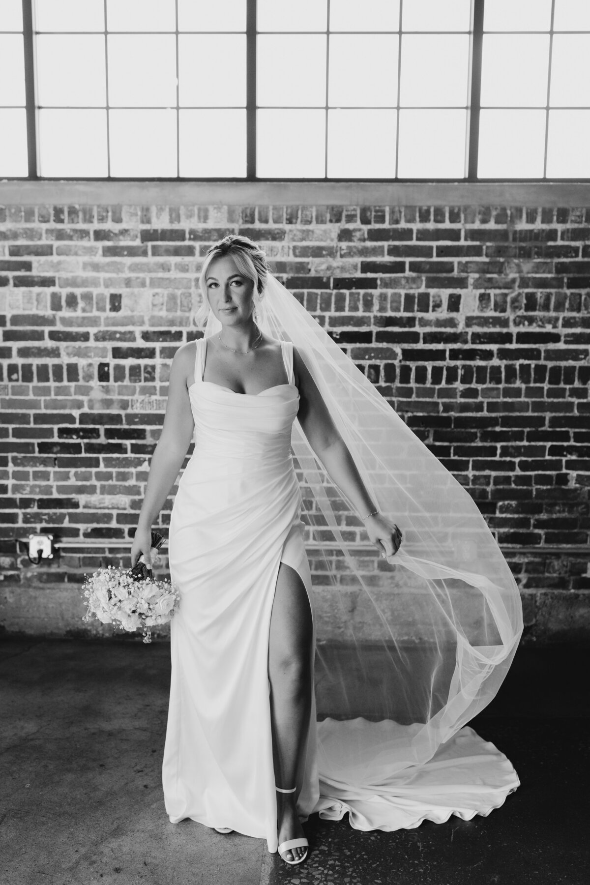 Bride posing with her veil flowing in a classic black and white wedding portrait.