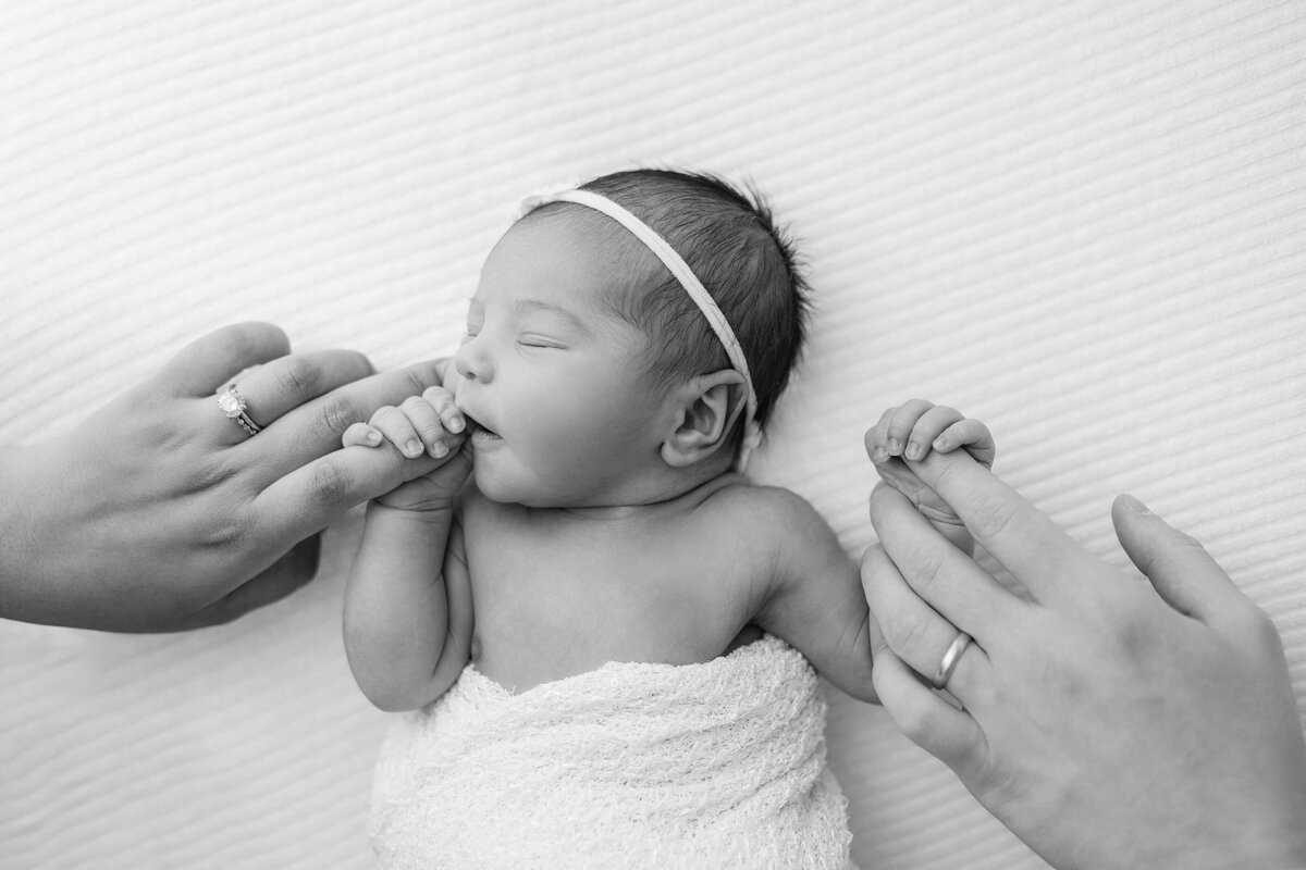 black and white film portrait of mom and dad holding their newborn daughter's hands