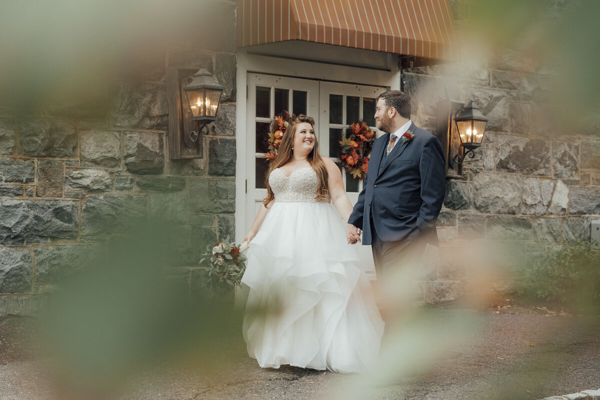 Smoke Rise Village Inn | Bride and groom walking holding hands by stone wall during fall wedding | Kinnelon, New Jersey