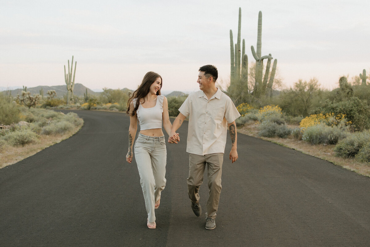 a couple walks on a road lined with cacti in the arizona desert at sunset