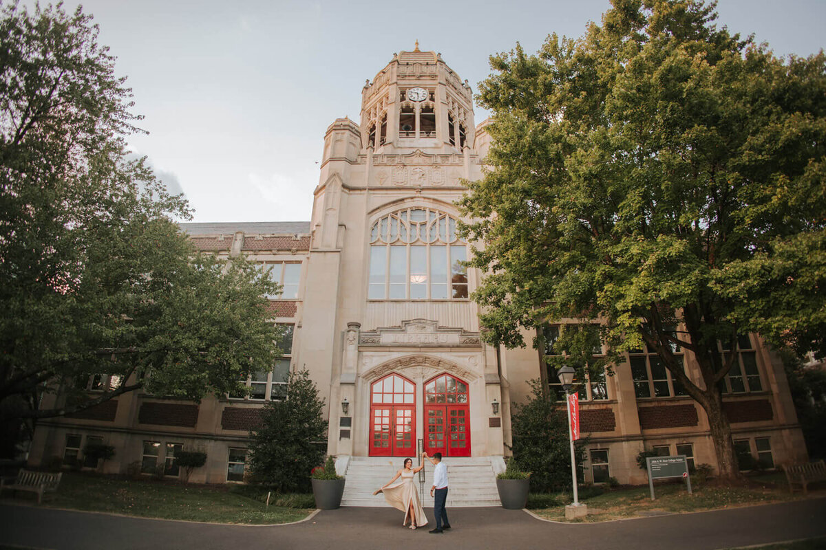 A couple dances in front of a historic building with red doors during their engagement session at Muhlenberg College.