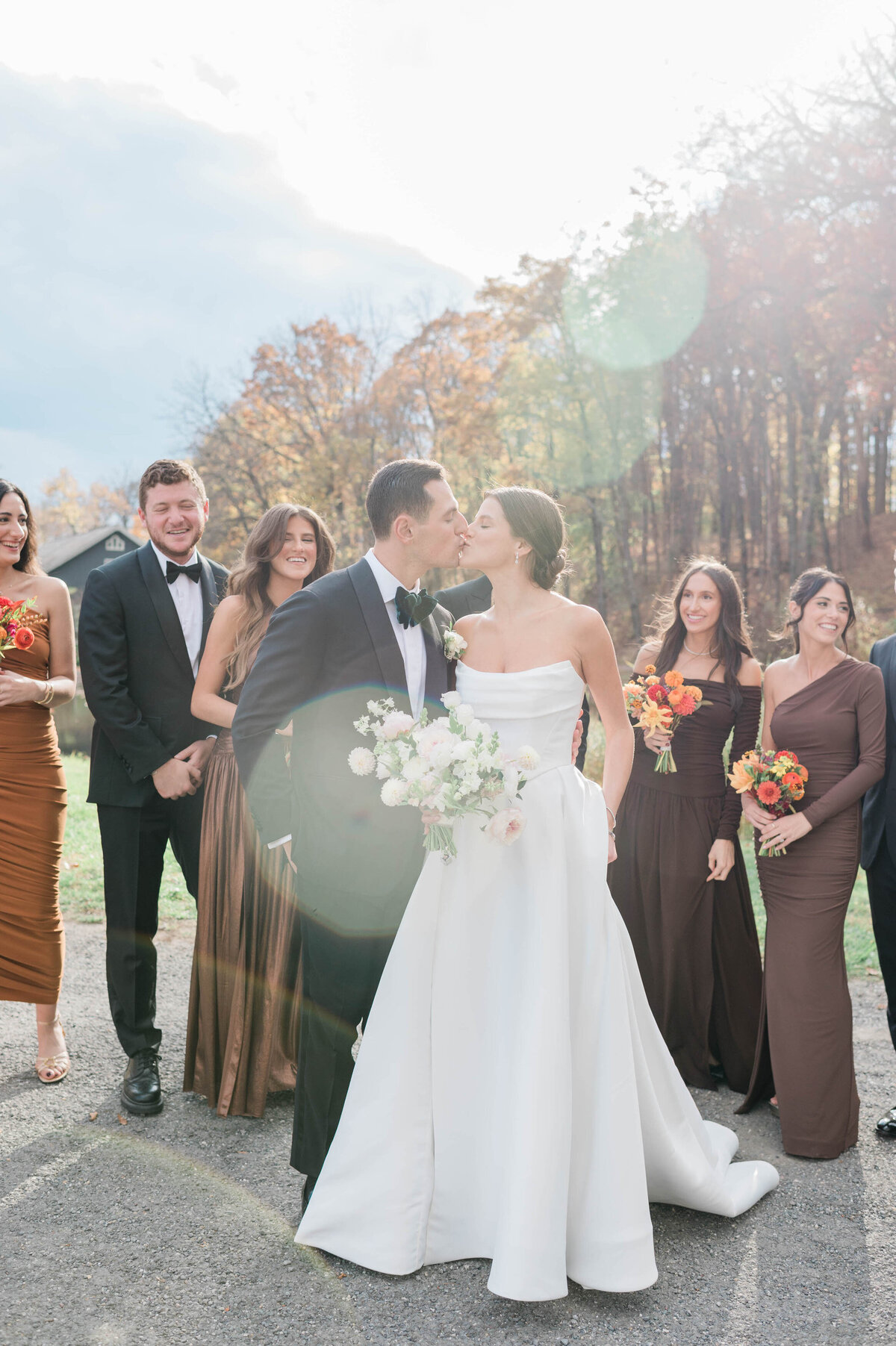 The newlyweds share a kiss outdoors, surrounded by their bridal party