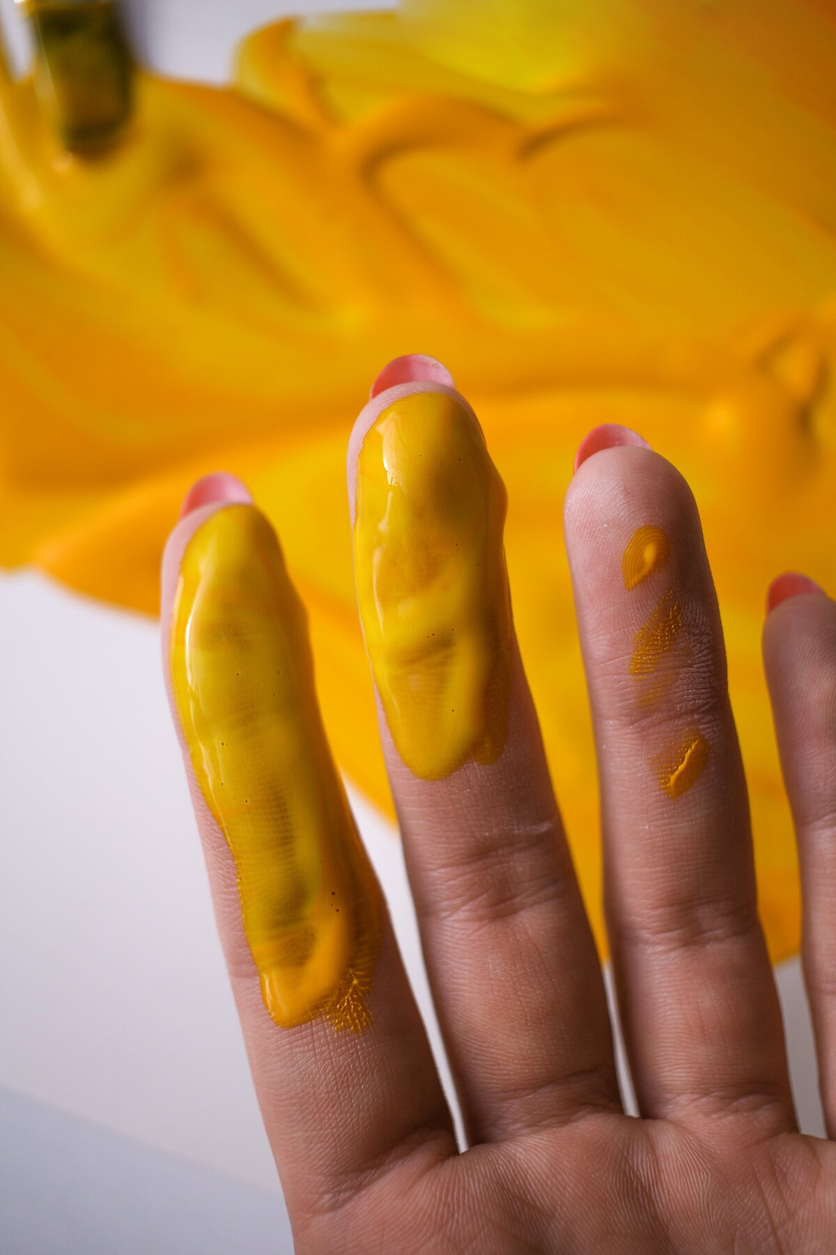 Fingers dipped in yellow paint are held up to the camera.