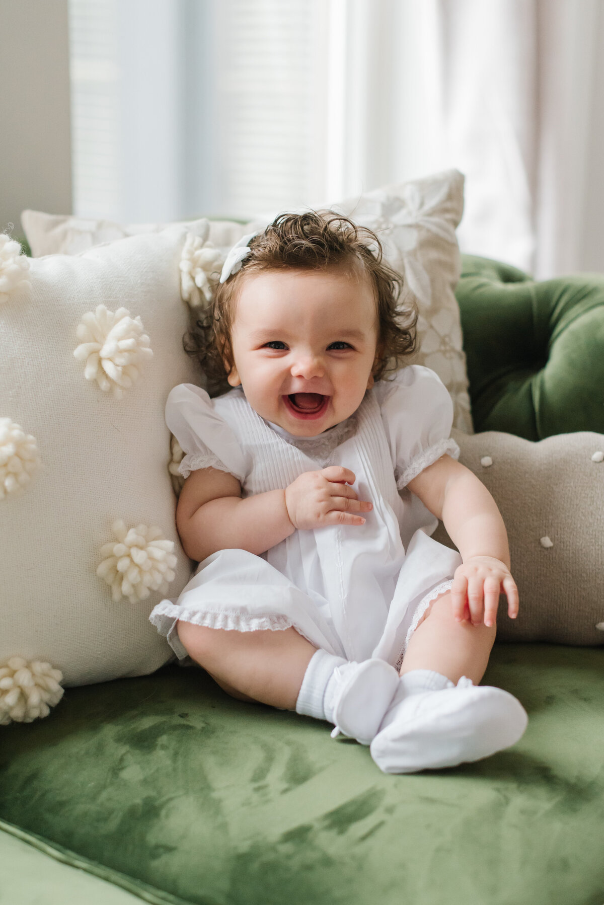 Baby giggling and sitting on green couch in white dress